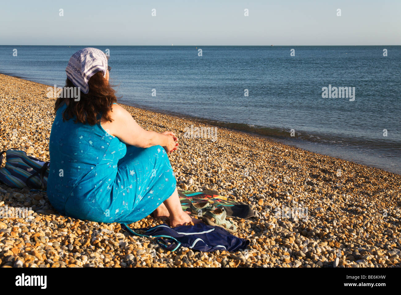 Une femme assise à contempler la mer tranquille sur la plage de Seaford, Sussex, England, UK. Banque D'Images