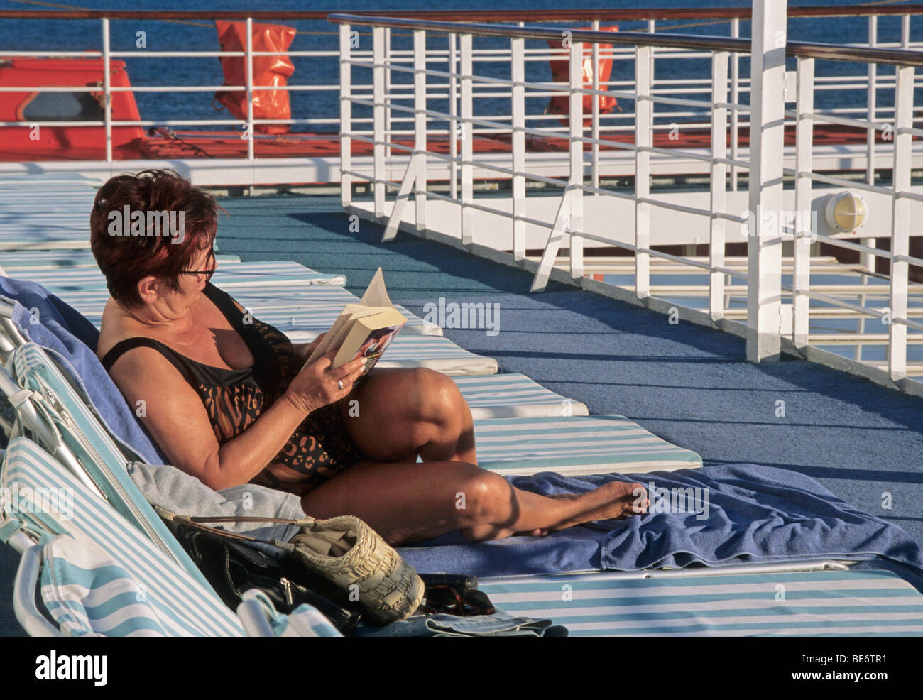 Dame de lire un livre sur une chaise longue sur le pont extérieur d'un bateau de croisière Banque D'Images