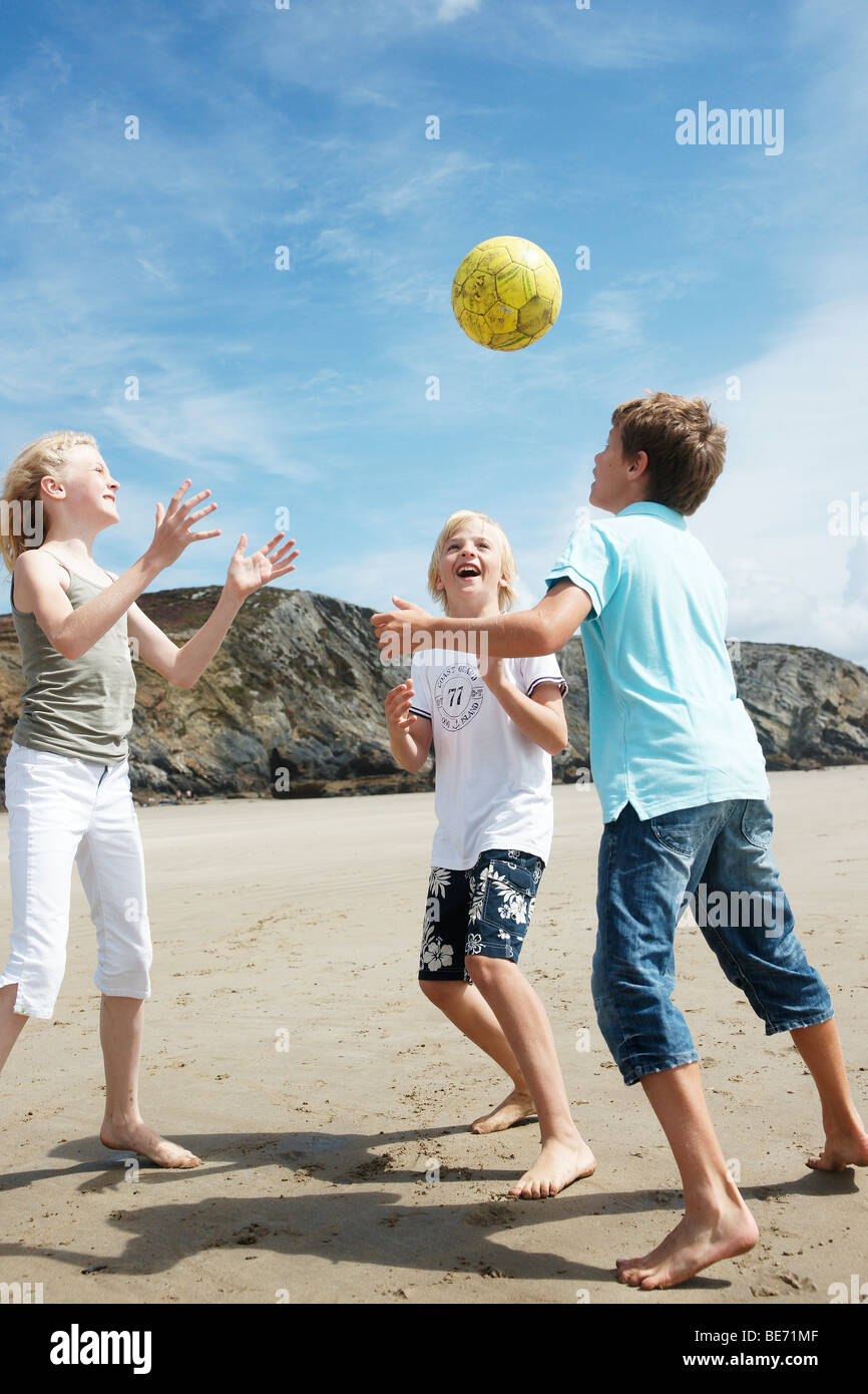 Deux garçons et une fille à jouer au ballon sur la plage, Bretagne, France, Europe Banque D'Images