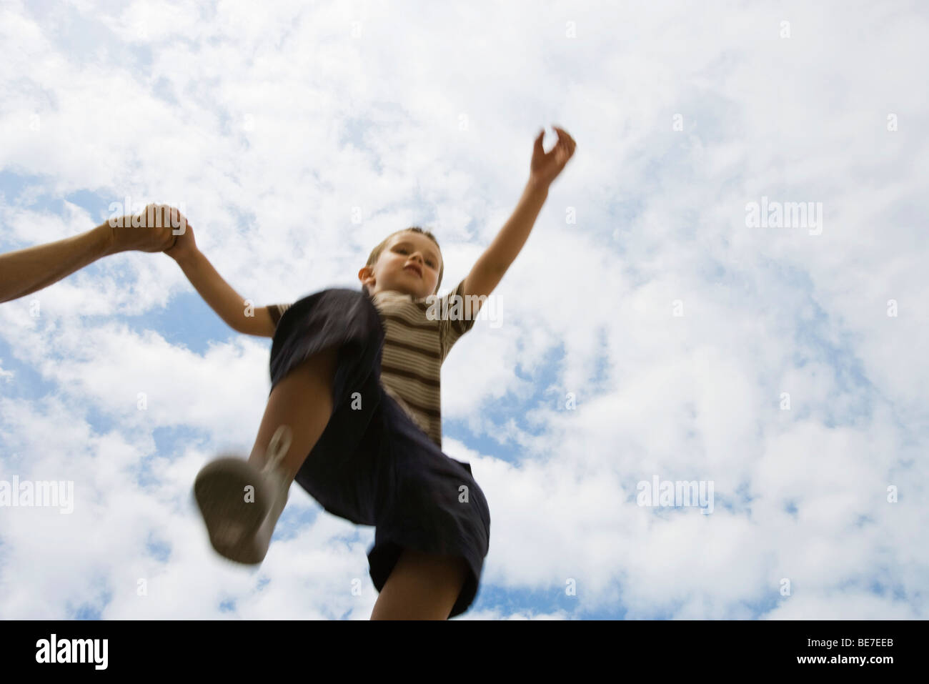 Boy holding mains adultes, sauter dans les airs, low angle view Banque D'Images