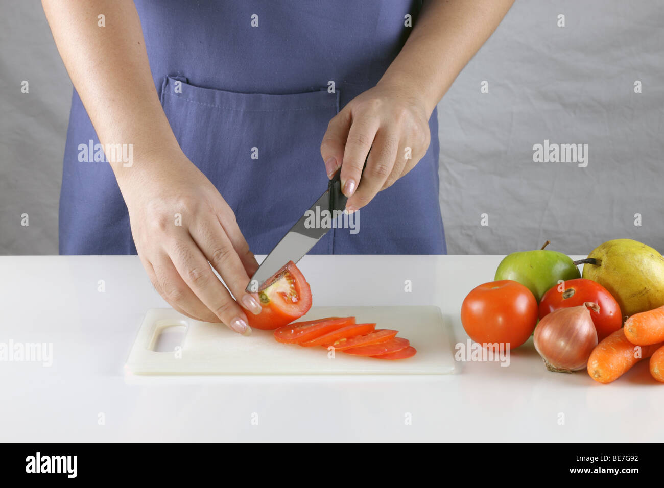 Une femme slicing tomatoes avec quelques fruits et légumes sur le côté Banque D'Images