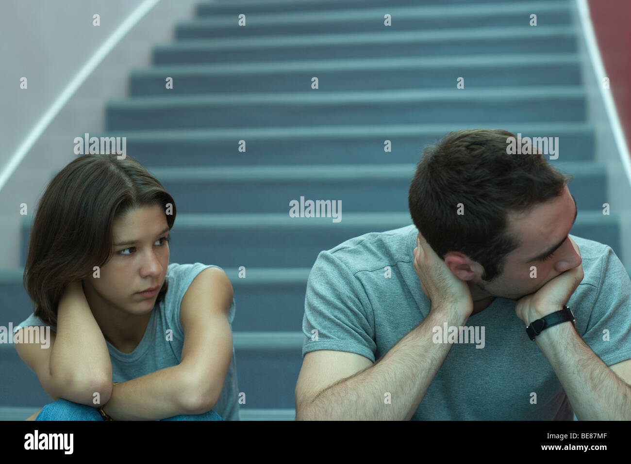 Young couple sitting on stairs, man holding head et à l'écart, regardant femme Banque D'Images