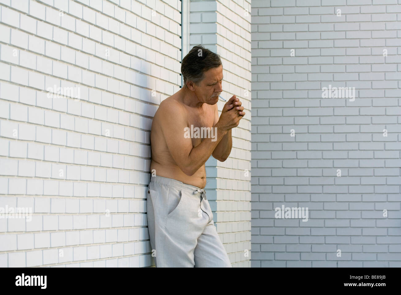 Torse nu man leaning against wall cigarette d'éclairage Banque D'Images