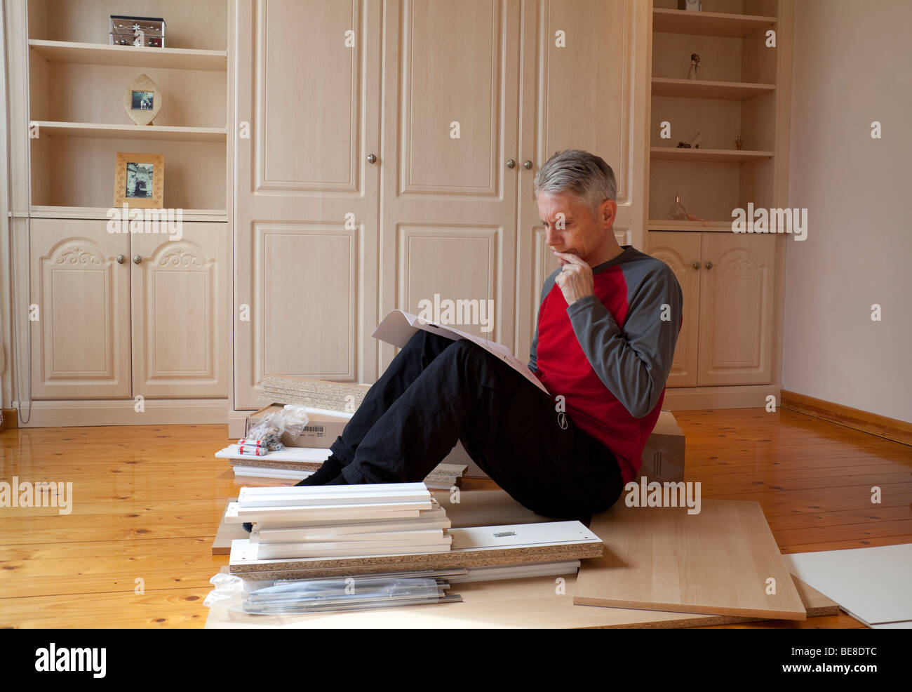 Vieil homme aux cheveux gris assis à la lecture perplexe notice entouré par flat pack meubles kit Banque D'Images