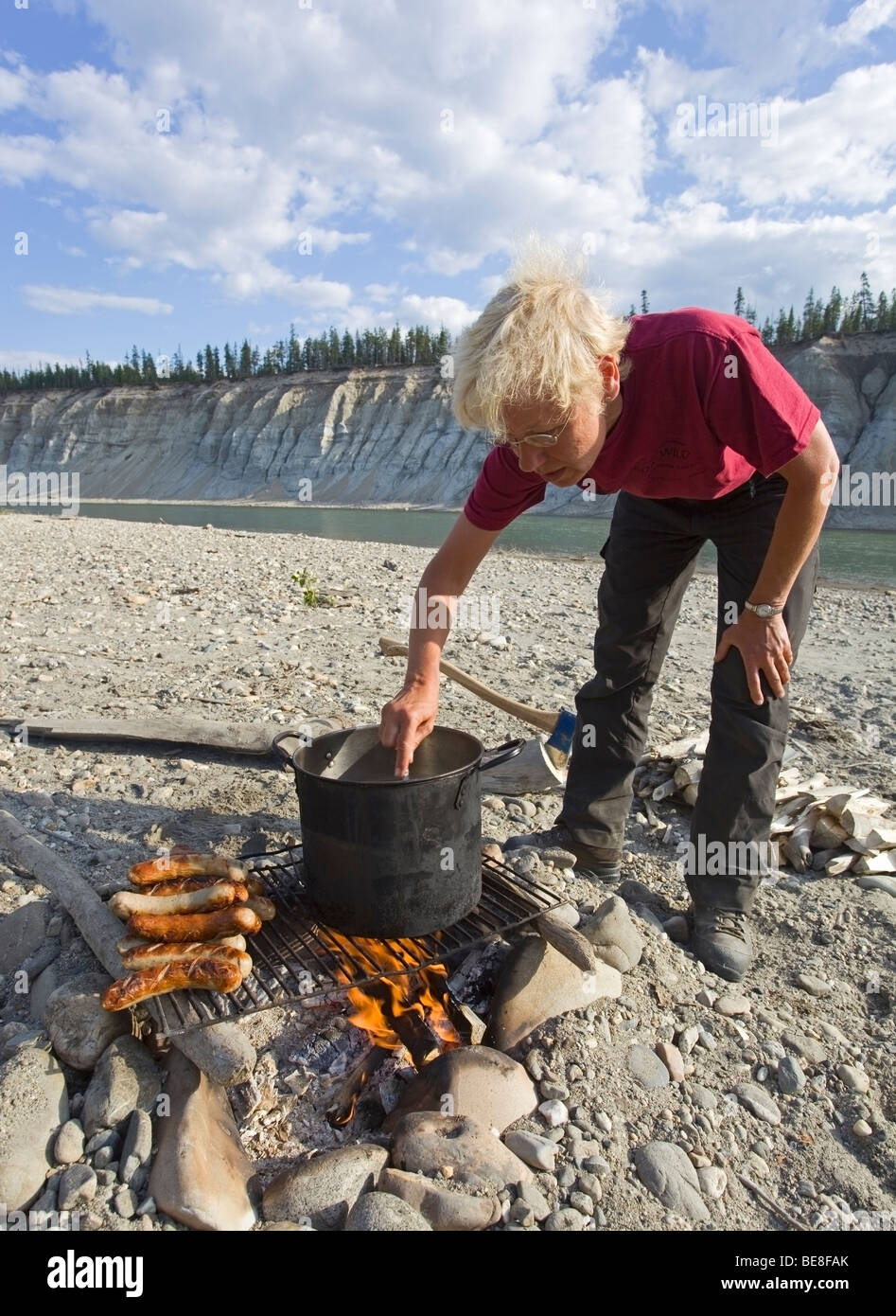 La cuisine femme sur un feu de camp, barbecue, saucisses Bratwurst, électrique, pot, grill, Upper Liard River, Yukon Territory, Canada Banque D'Images