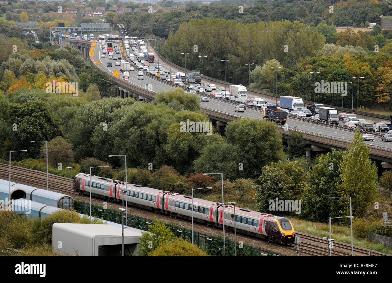Un train de banlieue EN MARCHE À CÔTÉ DE LA QUEUE LE TRAFIC SUR L'autoroute M6 Northbound élevée près de Birmingham, UK Banque D'Images
