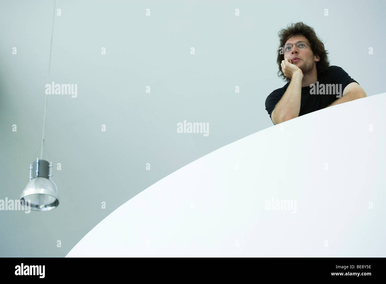 Jeune homme sur le balcon, se penchant sur le coude, low angle view Banque D'Images