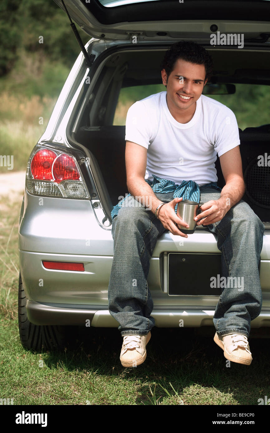 Young man sitting in car boot smiling at camera Banque D'Images