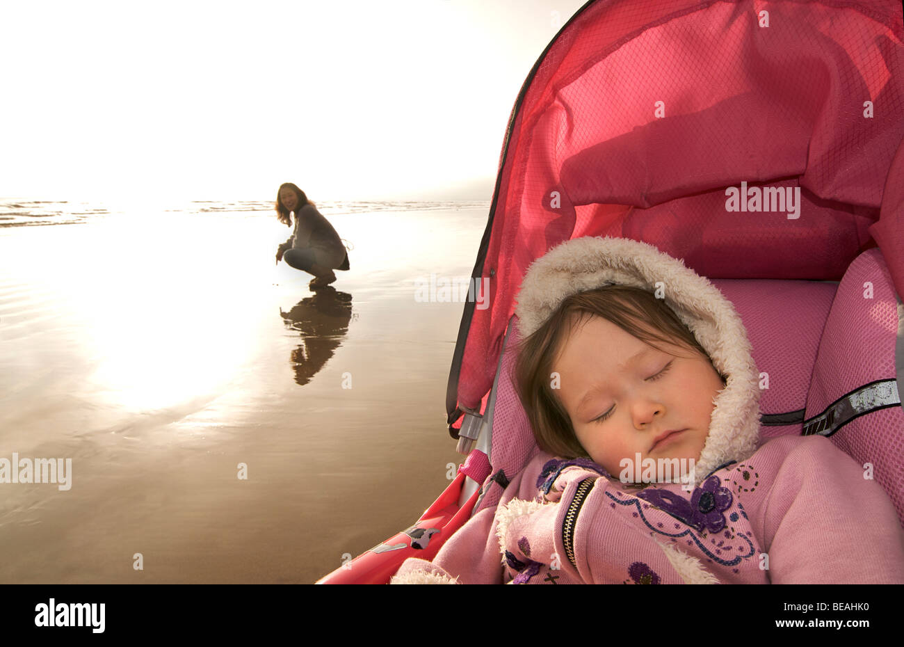 Enfant endormi dans la pram alors que mère bénéficie d'une promenade sur la plage. Banque D'Images