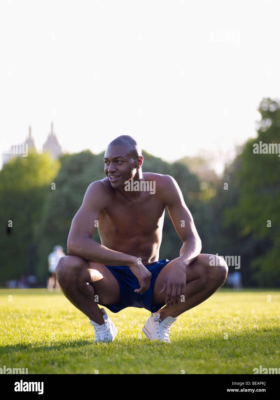 African man crouching in park Banque D'Images