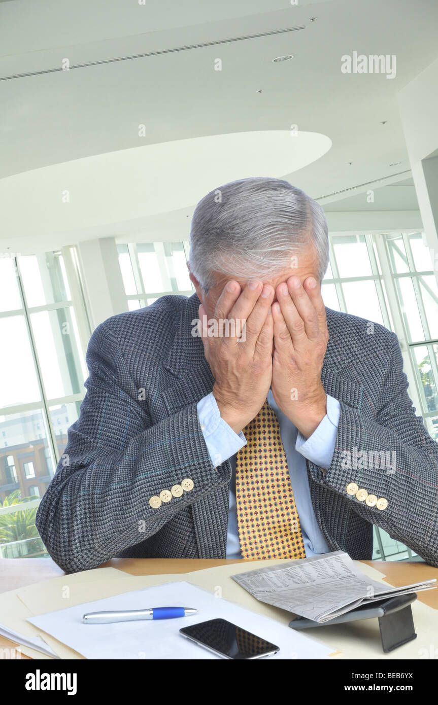 Mature Businessman assis à son bureau avec visage enfoui dans les mains Banque D'Images