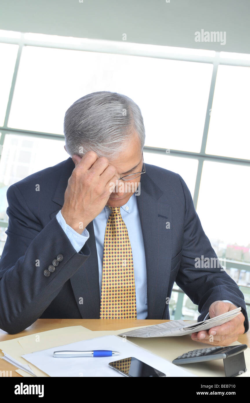 Businessman assis à son bureau dans un bureau moderne Reading Newspaper Banque D'Images