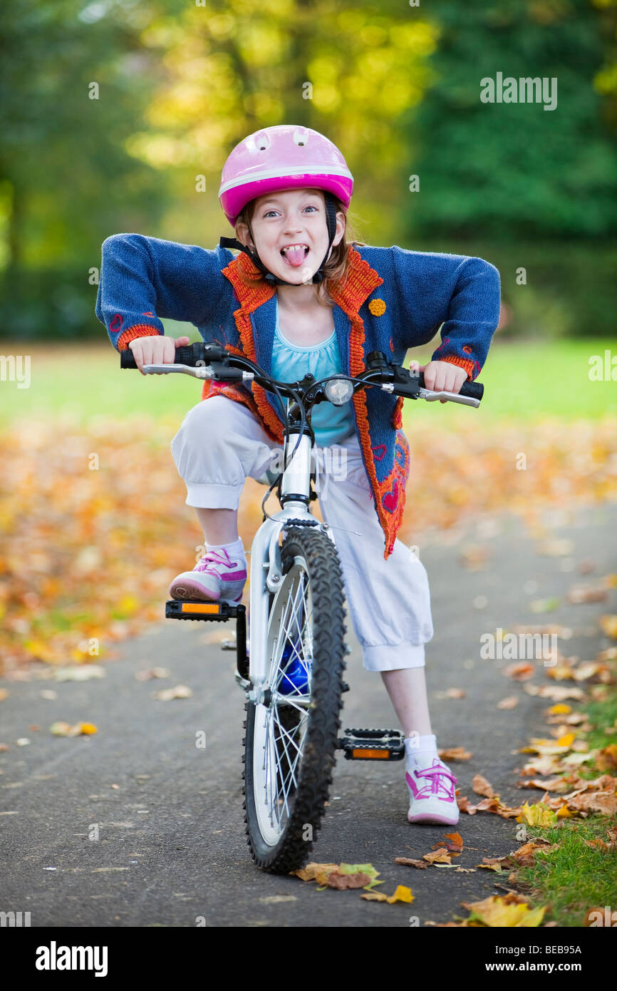 Jeune fille s'assit sur son vélo dans un parc en tirant une drôle de visage Banque D'Images
