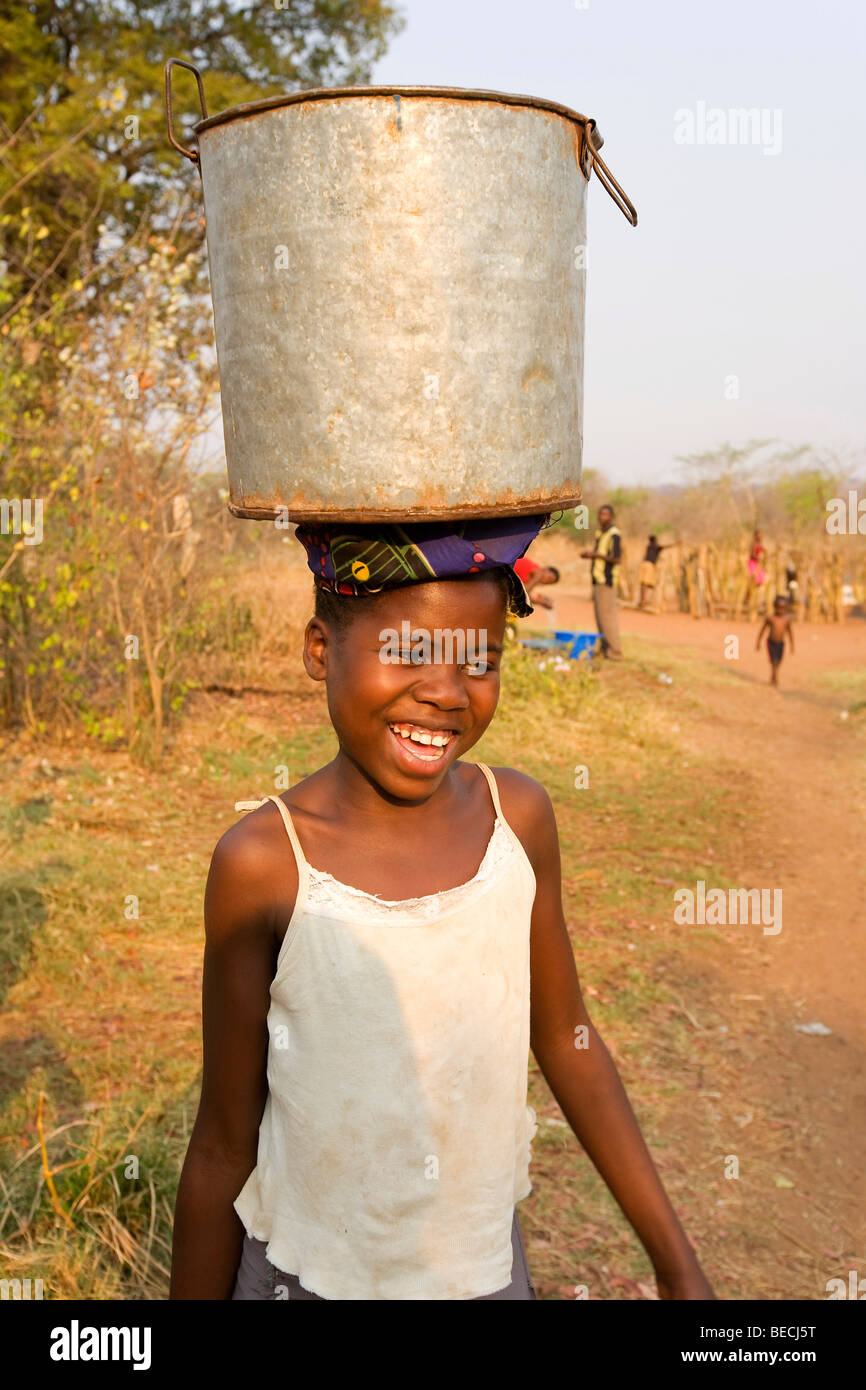 Jeune fille portant une cruche d'eau sur sa tête, African village Sambona, Province du Sud, République de Zambie, Afrique Banque D'Images