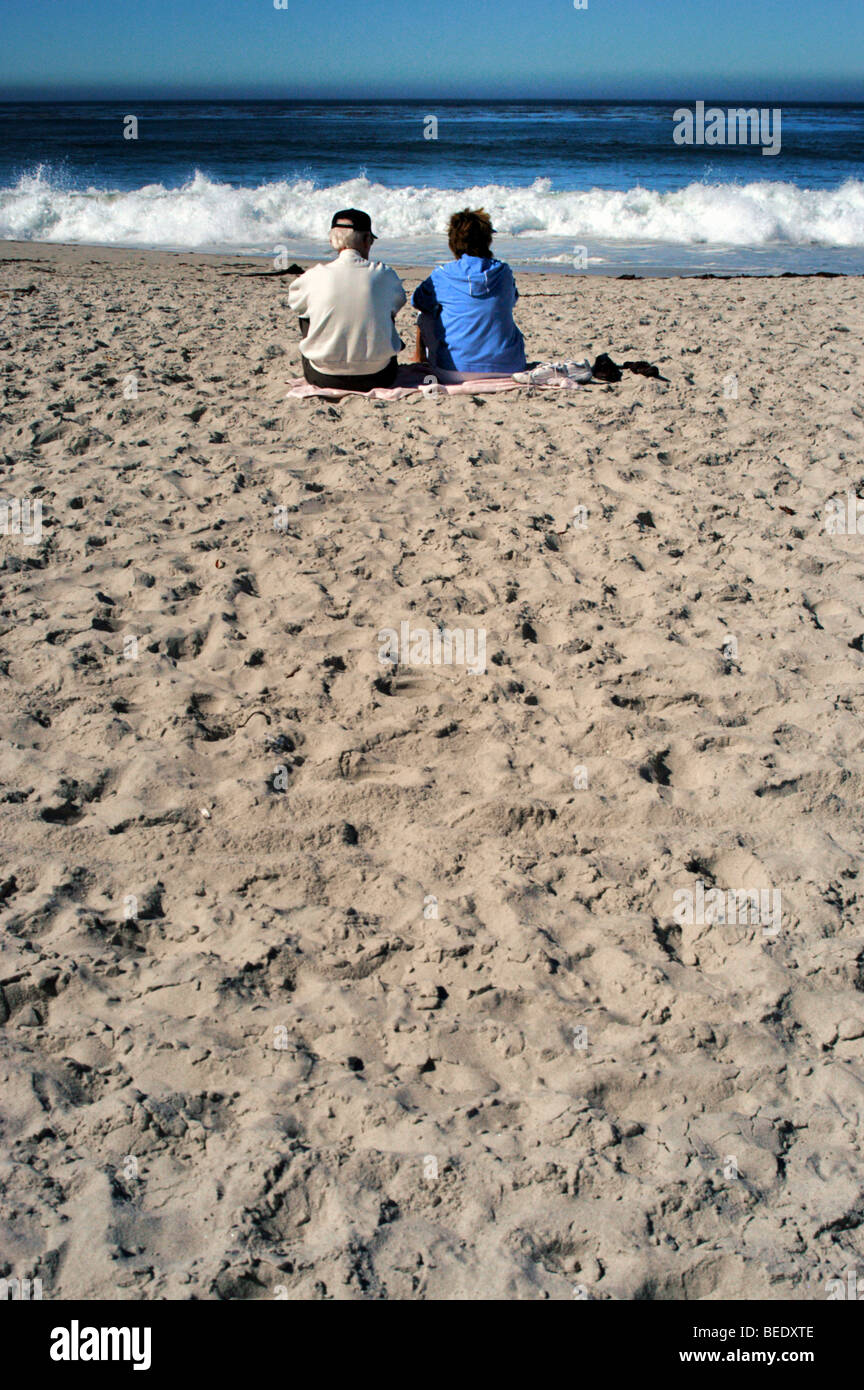 Couple assis sur une plage de sable immaculée regarder les vagues Banque D'Images