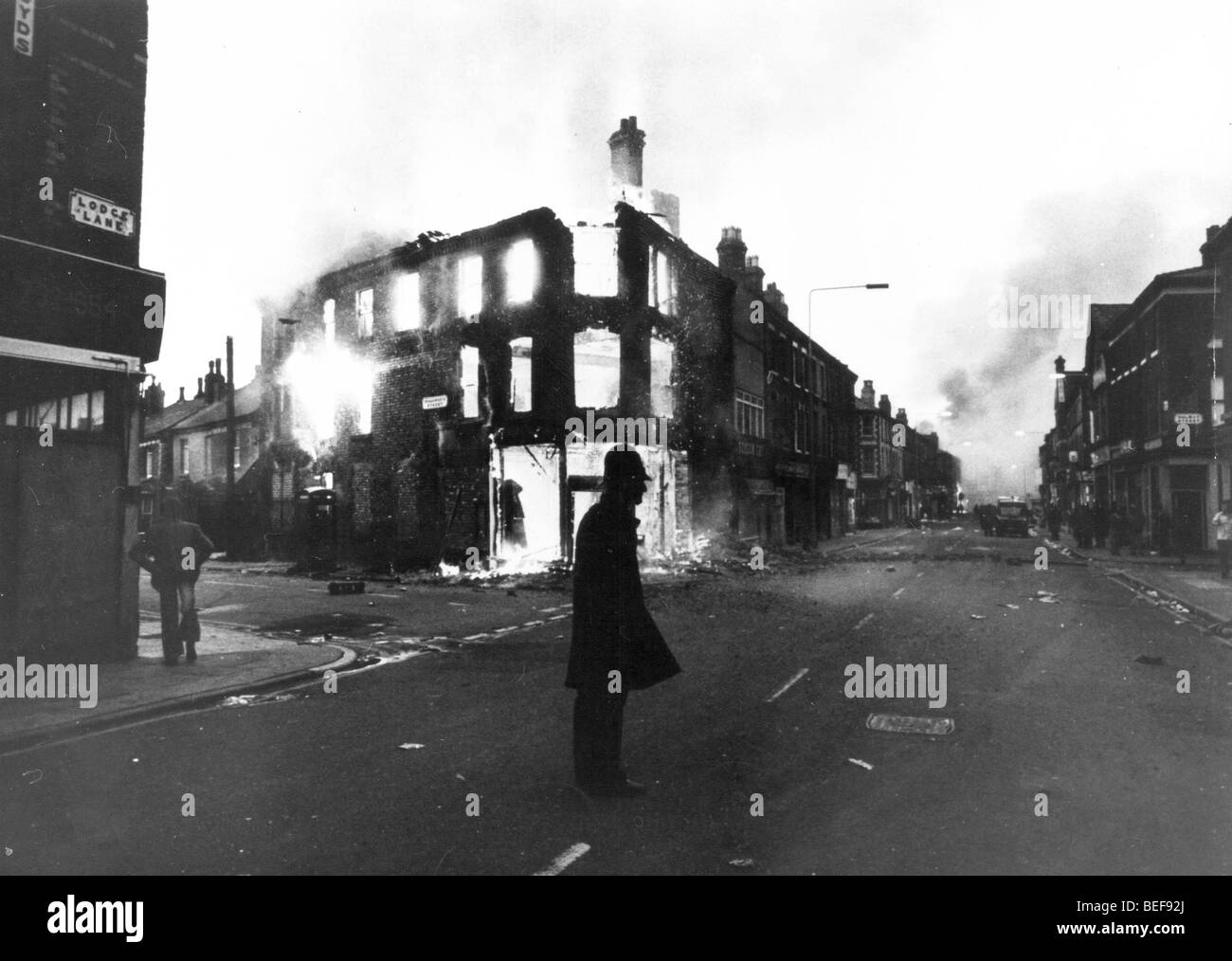 Flammes pour d'un bâtiment à Toxteth éviscéré, près de Liverpool avec un seul policier qui monte la garde après une longue nuit d'émeutes Banque D'Images