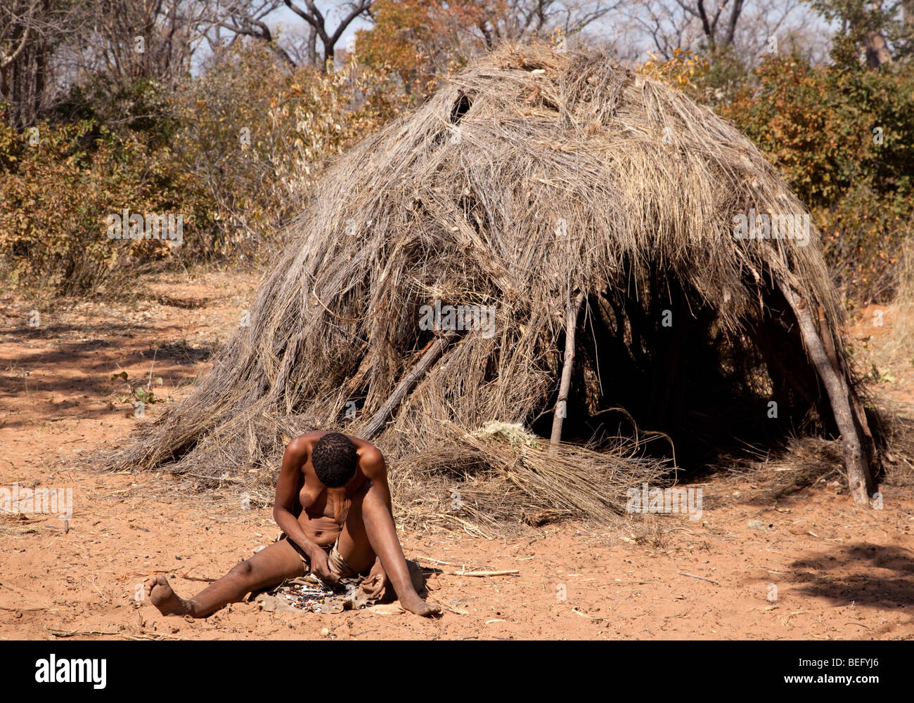 Village de San. Femme assise à l'extérieur de San une hutte d'herbe. Banque D'Images