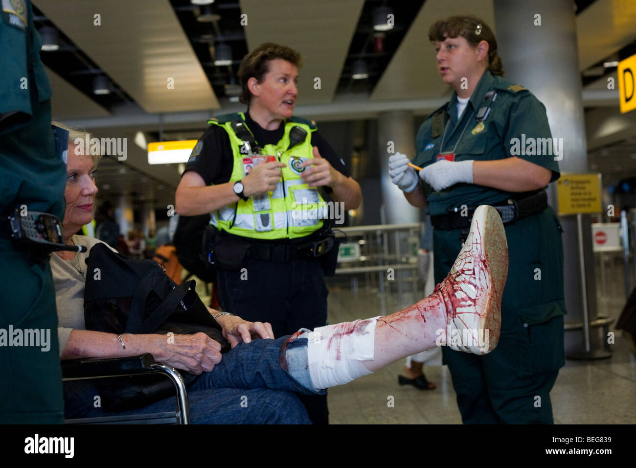Les intervenants paramédicaux NHS assiste à une dame passager dans le terminal 3 d'Heathrow qui a trébuché et mal gashed sa jambe. Banque D'Images