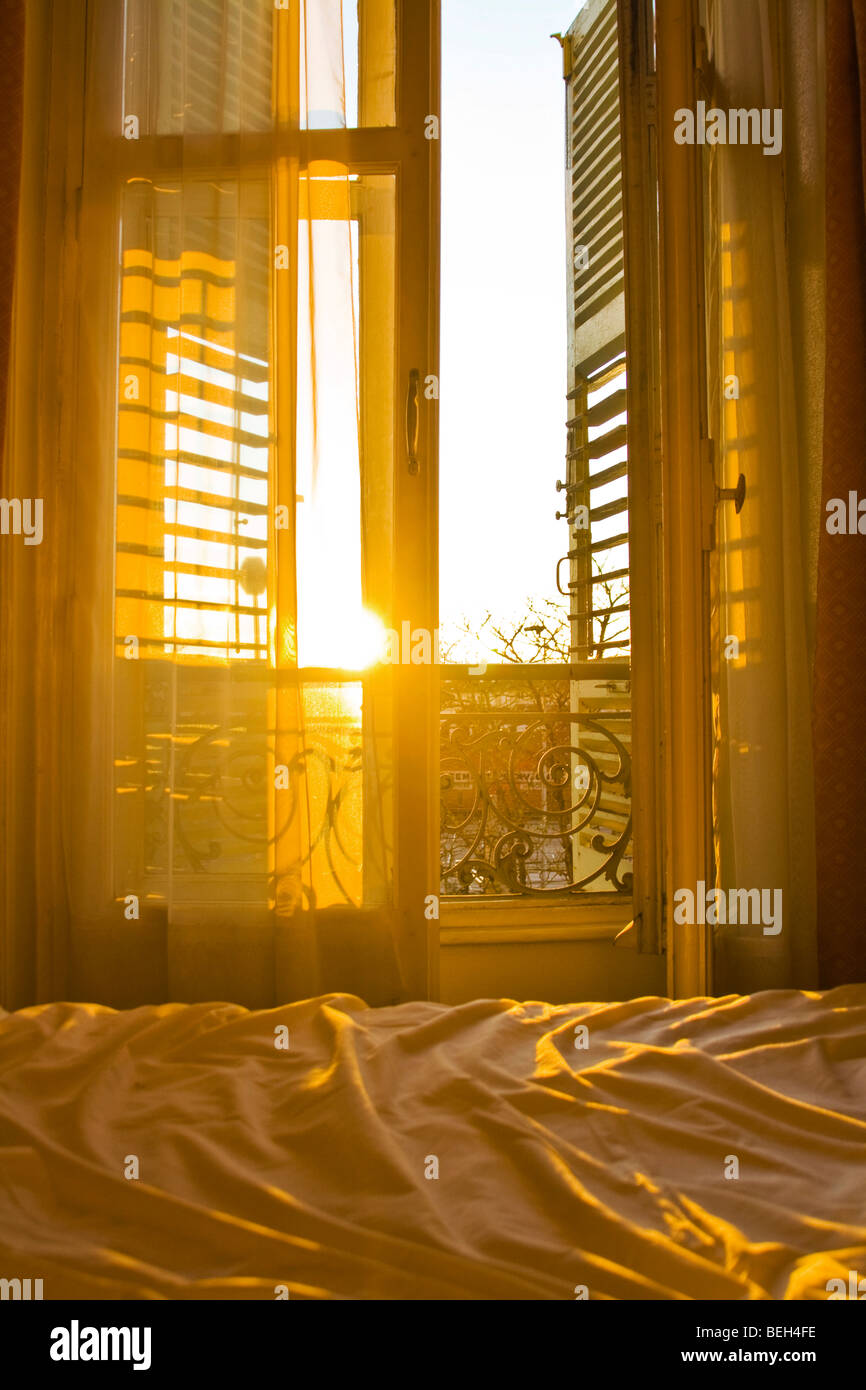 Lever du soleil à travers les volets d'une chambre d'hôtel parisain, illuminant le lit défait Banque D'Images