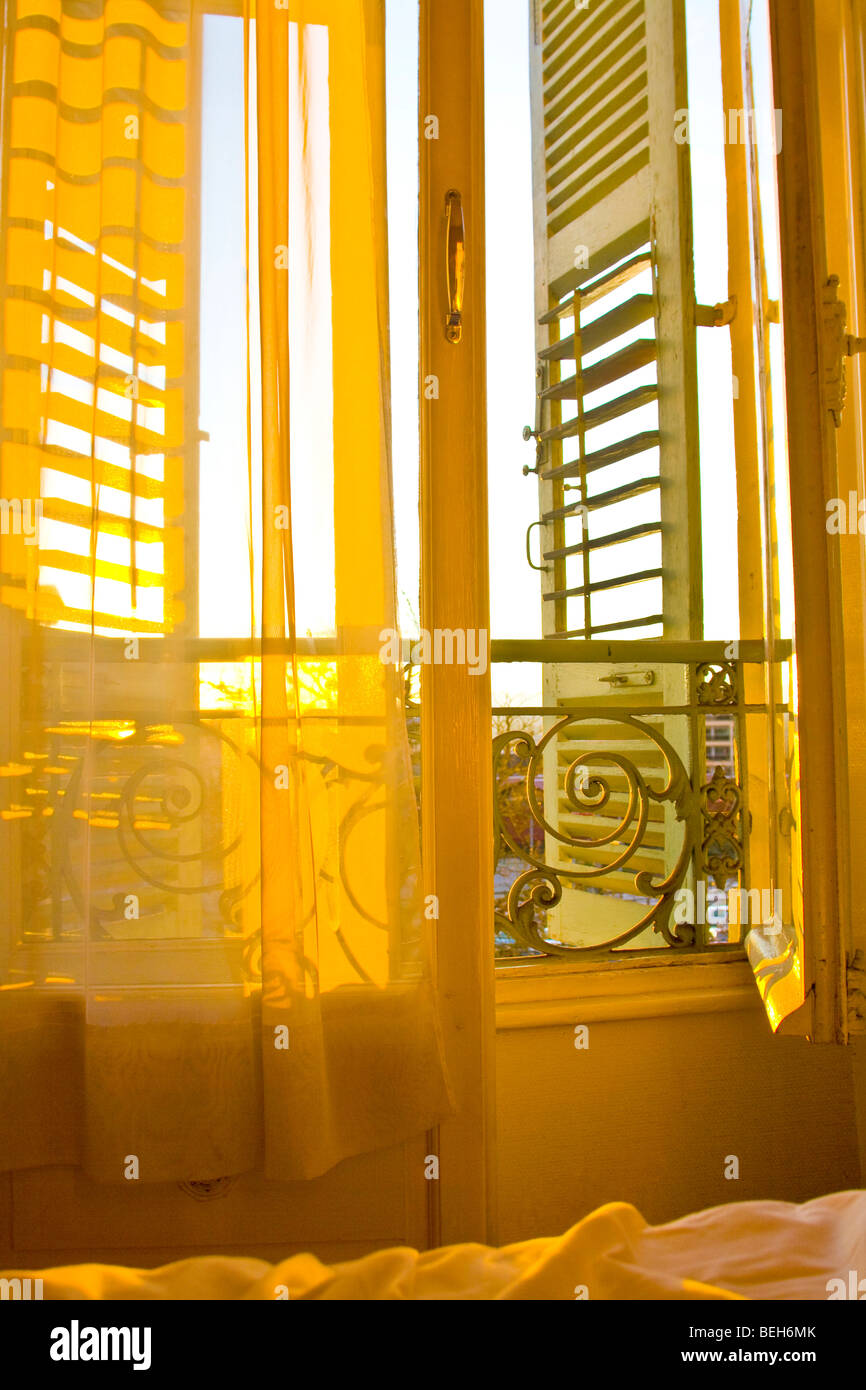 Lever du soleil à travers les volets d'une chambre d'hôtel parisain, illuminant le lit défait Banque D'Images