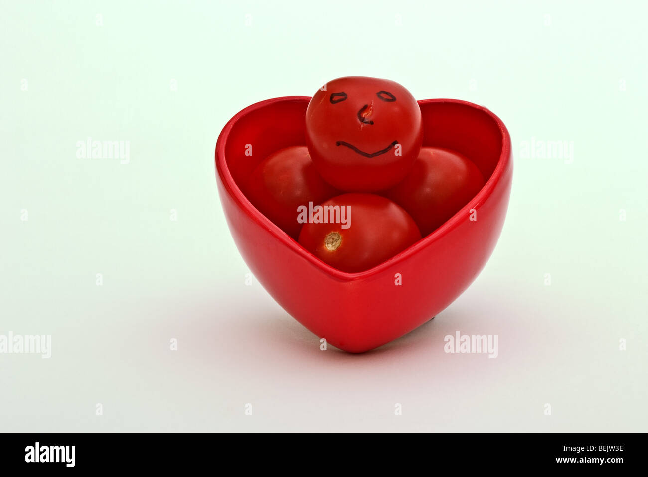 En forme de coeur rouge dur rempli de tomates mûres, un bébé avec un smiley. Banque D'Images