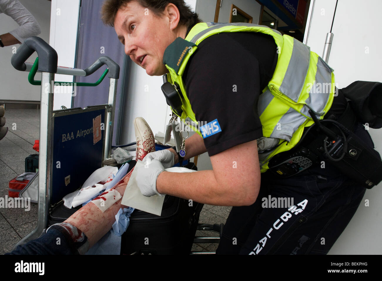 Un paramédic femelle aide une dame passager dans l'aéroport d'Heathrow Terminal 3 qui a trébuché sur les escaliers roulants, très gashing sa jambe. Banque D'Images
