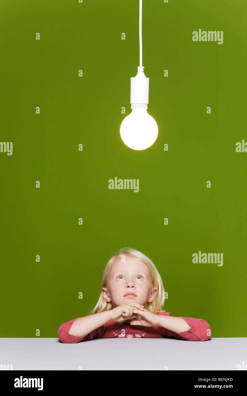 Petite fille qui envisagent l'ampoule lumineuse suspendue au-dessus Banque D'Images