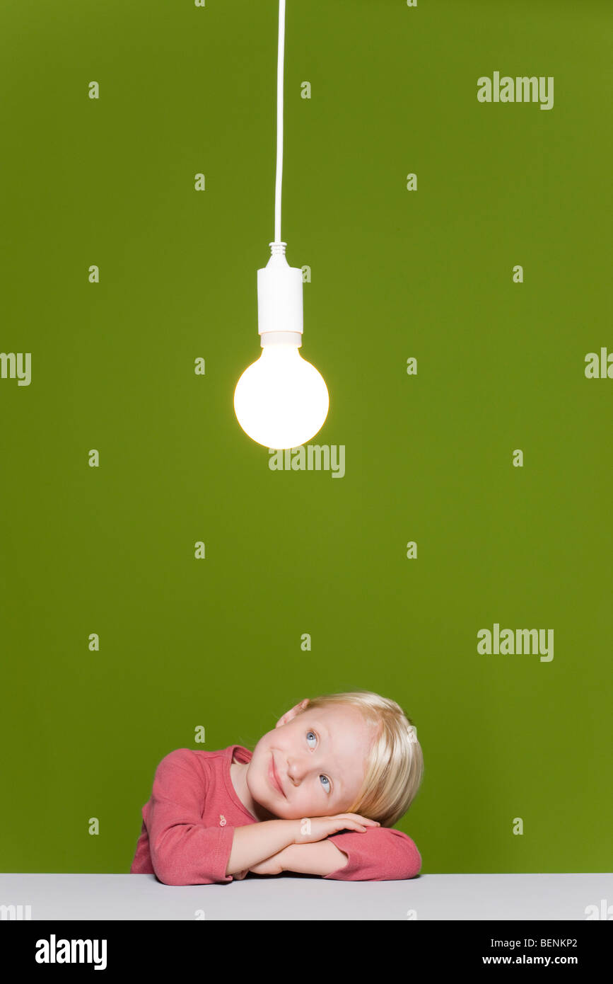 Little girl resting head on arms qui envisagent l'ampoule lumineuse suspendue au-dessus Banque D'Images