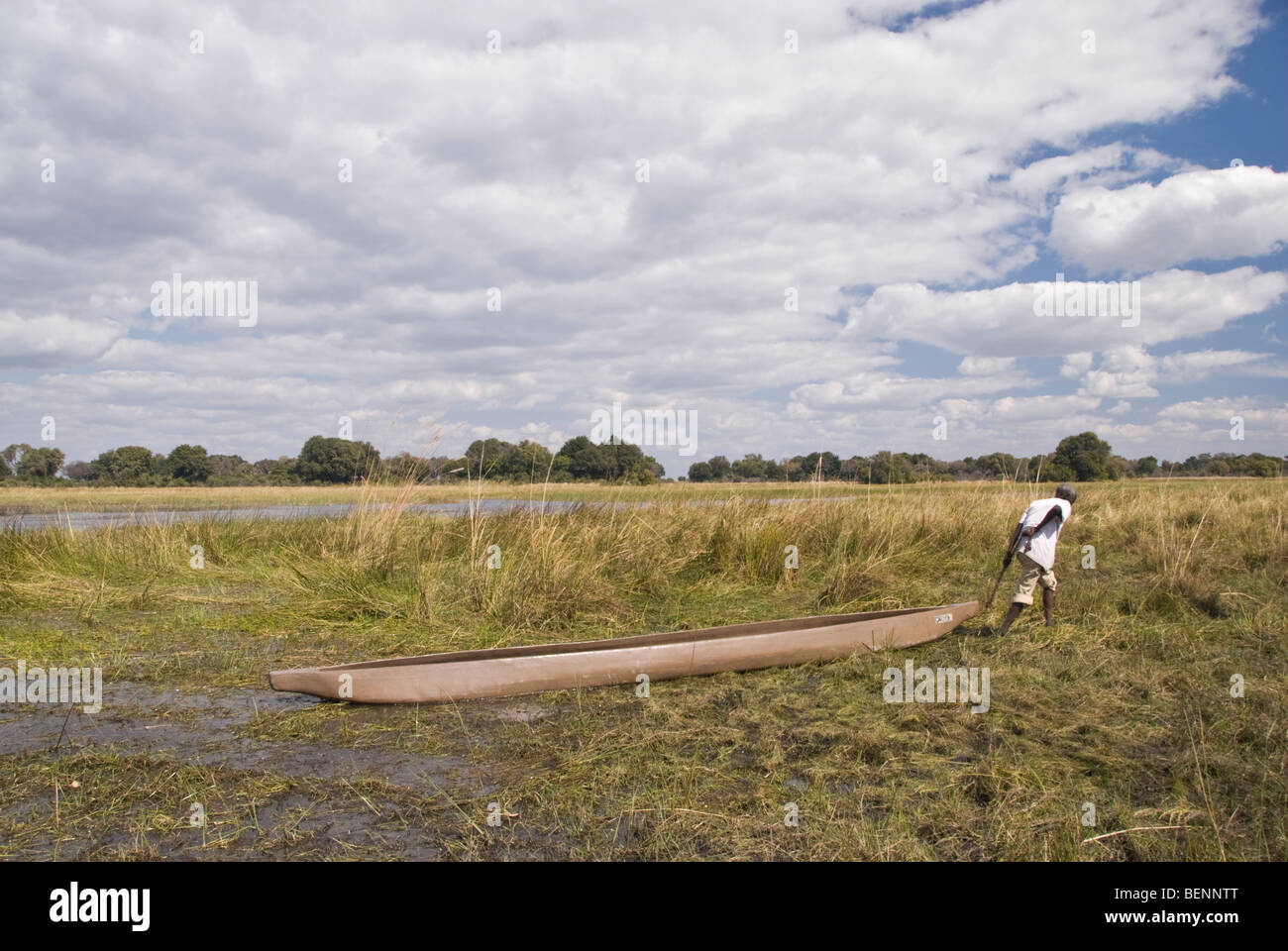 Mokoro poler portant son bateau sur une journée nuageuse. Delta de l'Okavango, au Botswana, l'Afrique. Banque D'Images