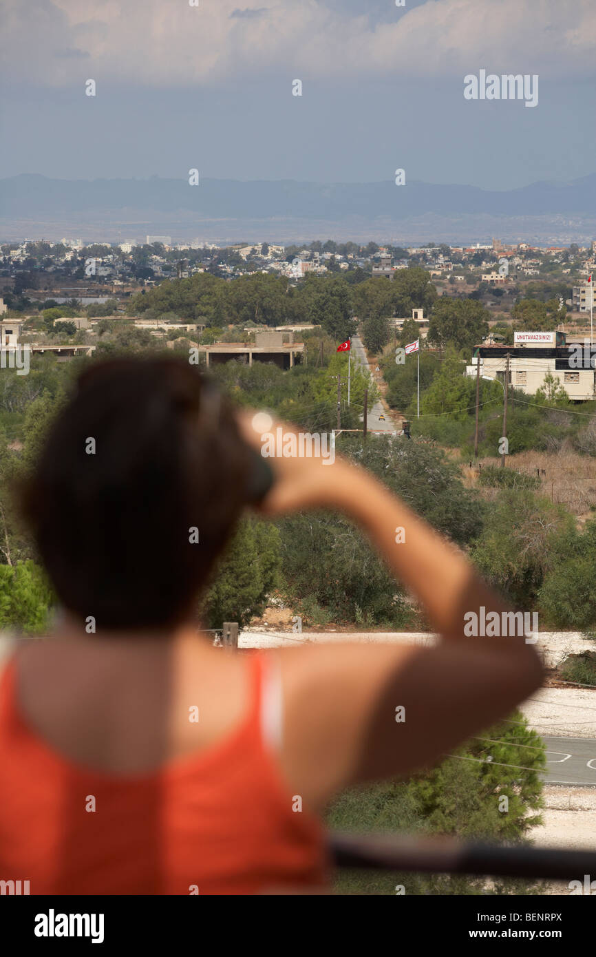 Femme tourist en utilisant des jumelles pour donnent sur la zone tampon des Nations Unies dans la ligne verte divisant le nord et le sud de Chypre à Famagouste Banque D'Images