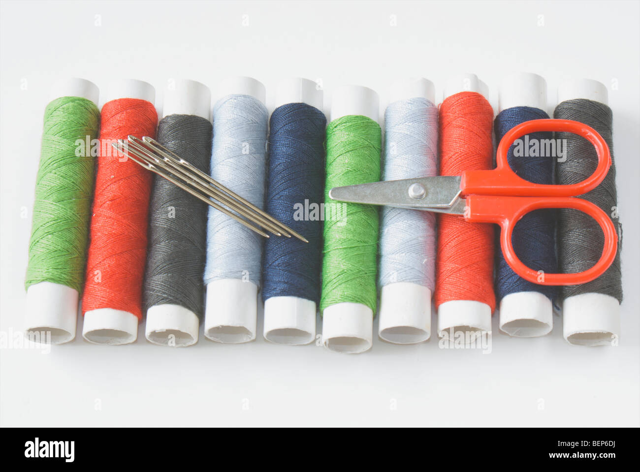 Des bobines de fil colorés avec des aiguilles et des petits ciseaux sur un fond blanc. Banque D'Images