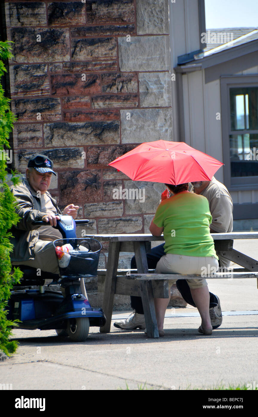 Les personnes âgées à table de pique-nique avec parapluie rouge pour bloquer les rayons UV Banque D'Images