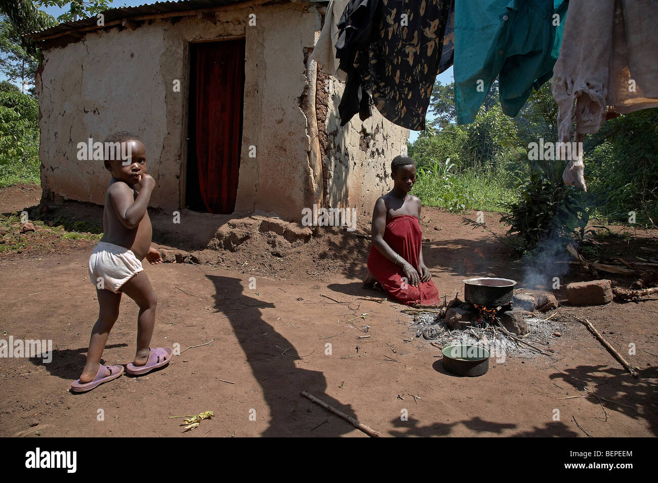 L'Ouganda, une jeune femme Proscovia, et son bébé Saifa (3), la cuisson sur un feu ouvert en face de sa petite chambre. Kayunga District. Banque D'Images