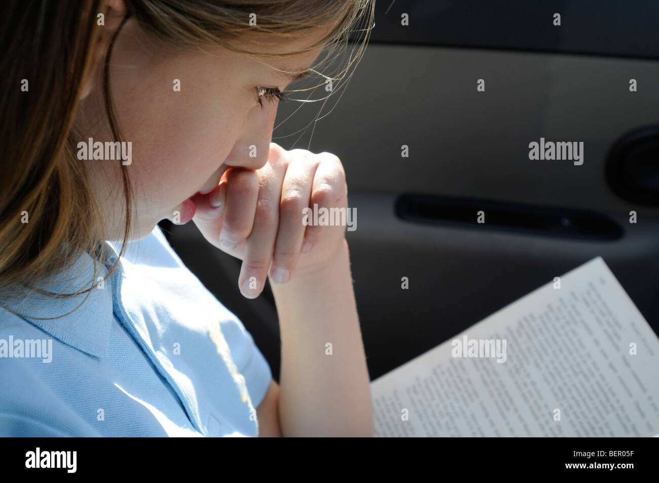 Une fillette de 9 ans dans son uniforme scolaire se lit dans une voiture en stationnement. Banque D'Images