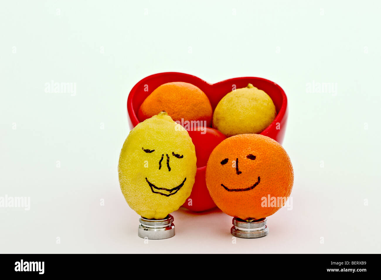 En forme de coeur rouge bol rempli d'un bébé, une orange mûre keylime, et une petite tomate. Entouré de smileys Banque D'Images