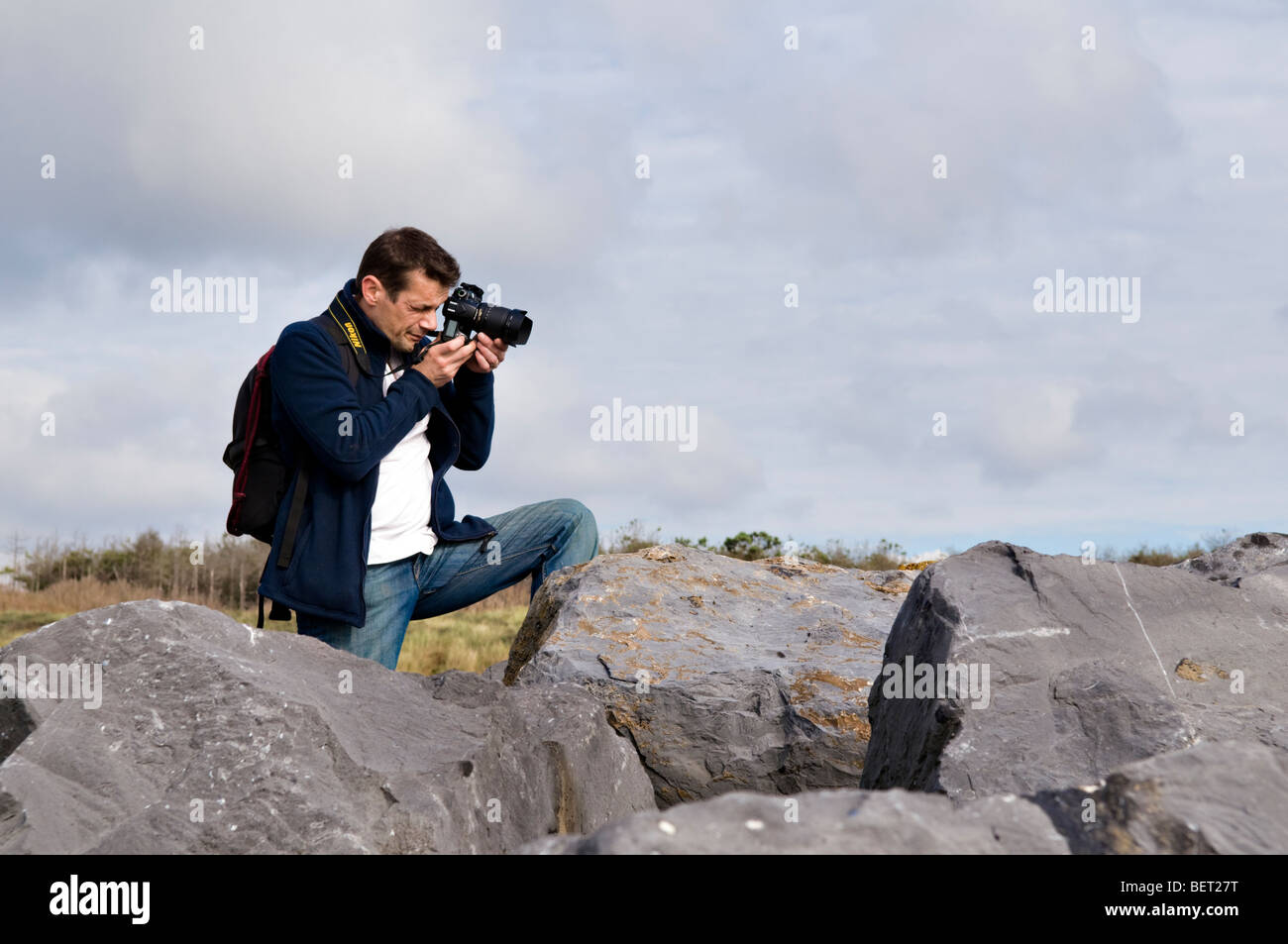 Photographe des hommes à prendre des photos sur les roches à Pembrey plage, Mid Wales à l'aide d'appareil photo Nikon Banque D'Images