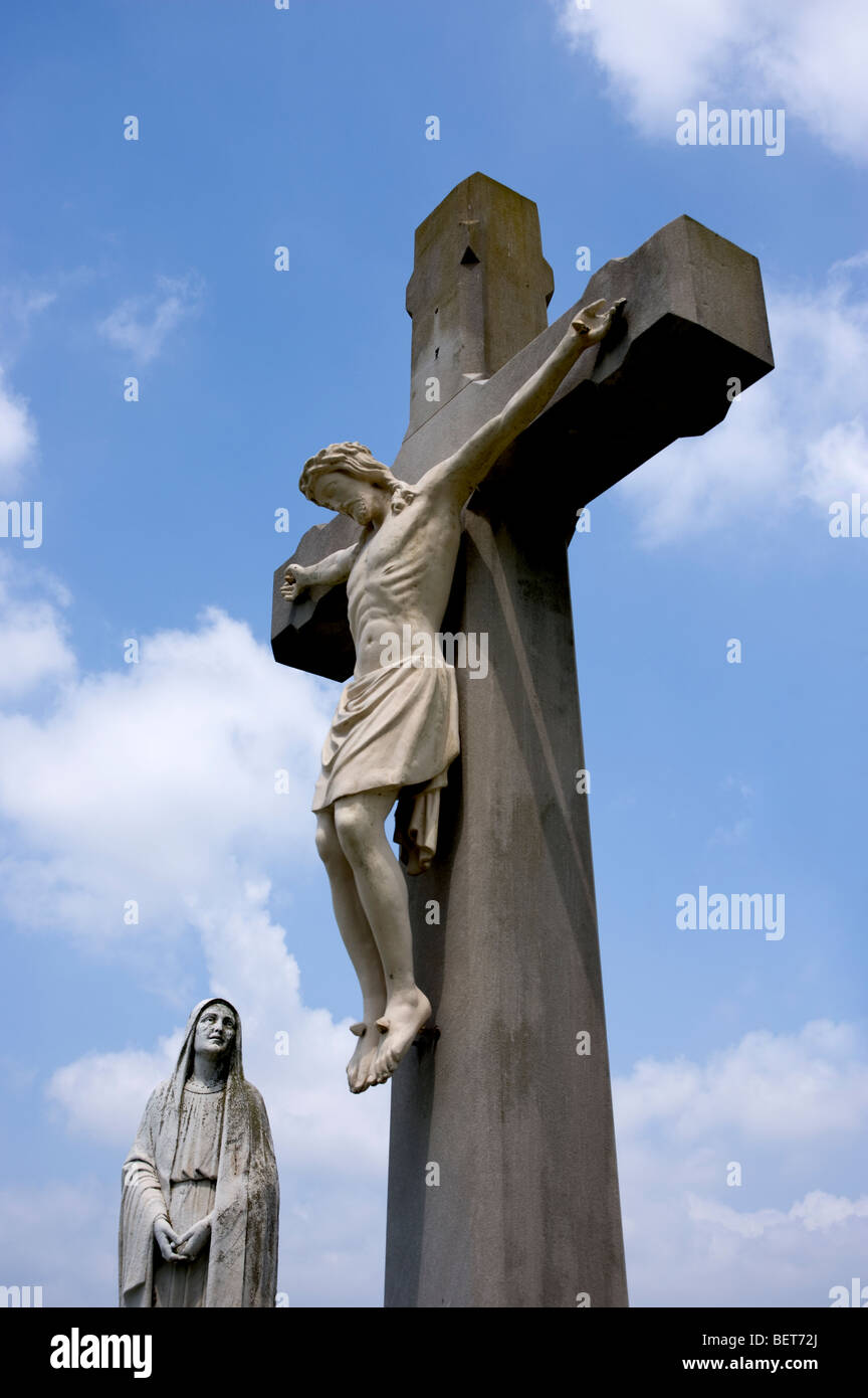 Mère Marie se penche sur la Croix comme Jésus il se bloque sur la tombe de prêtres locaux dans un petit, rural, Catholique grave yard. Banque D'Images