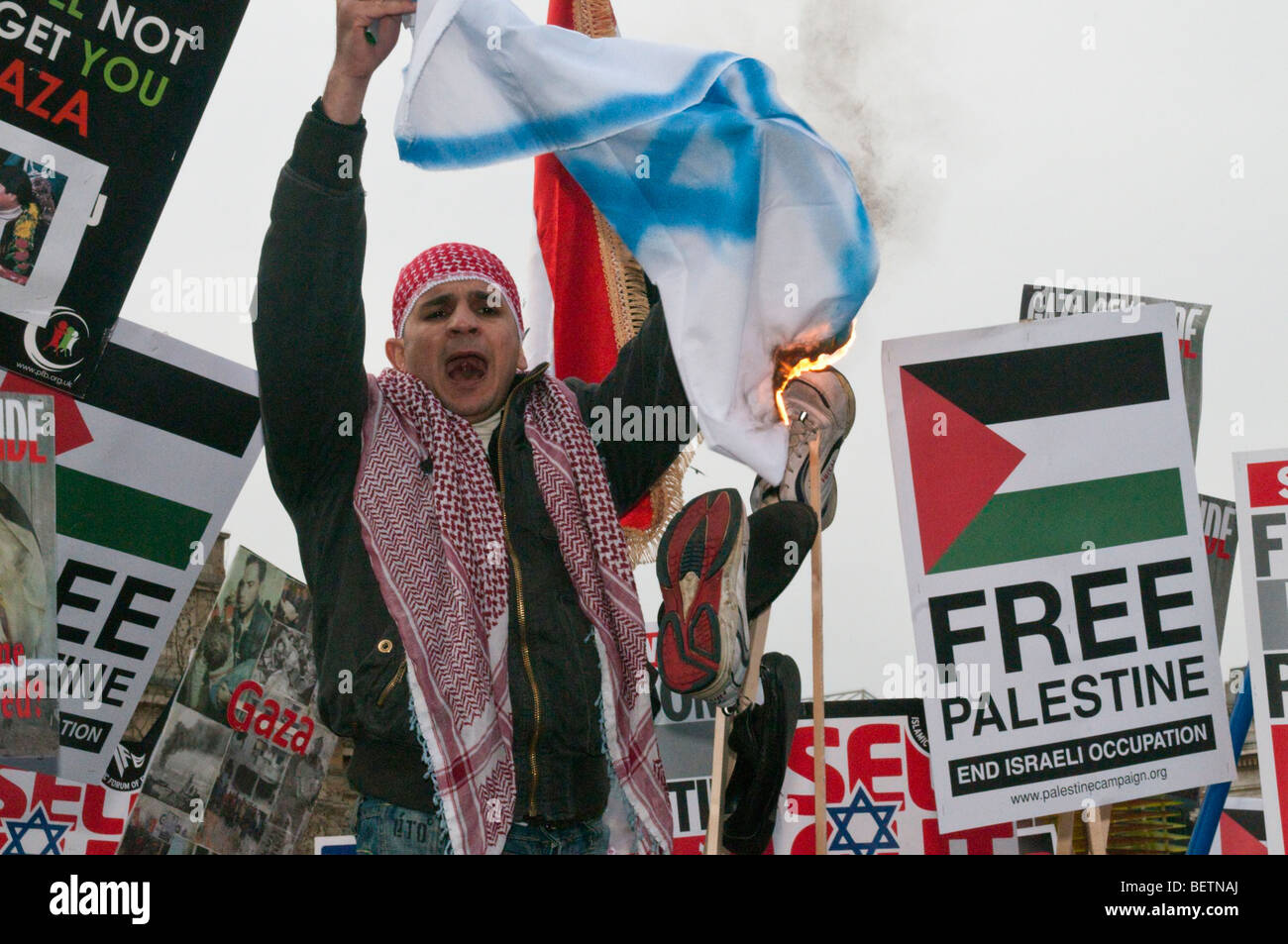 Gaza - 1000 morts et rien dit de démonstration. Homme avec bonnet et écharpe palestinienne brut burns drapeau israélien. Trafalgar Square Banque D'Images