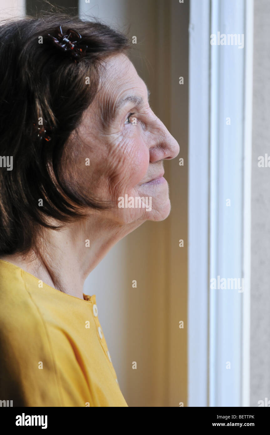 Concept - triste solitude 80s senior woman looking through window at home Banque D'Images