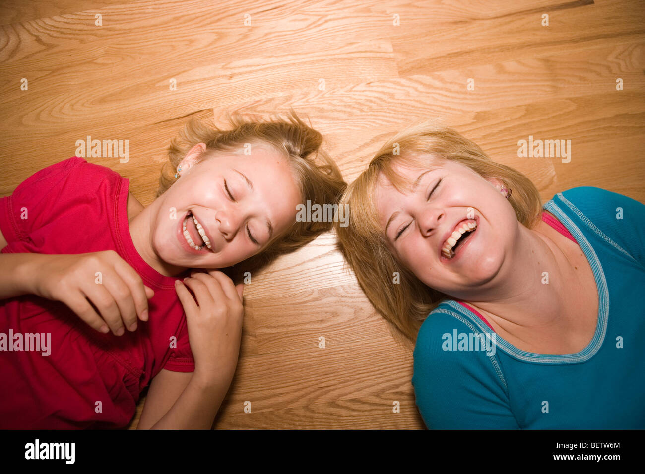 Deux sœurs de rire hystériquement sur un plancher de bois, âgés de 11 et 14 Banque D'Images