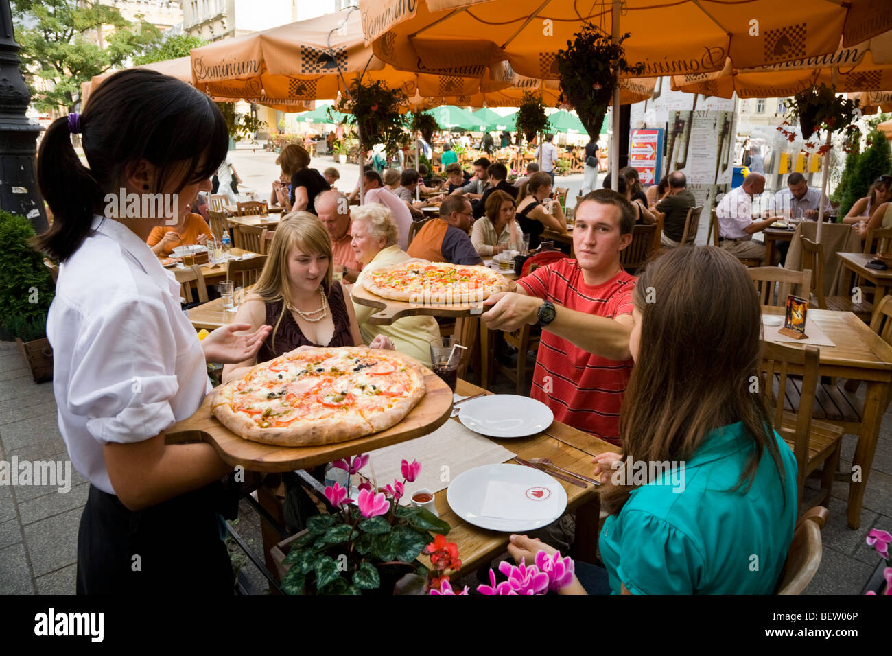 Serveuse sert des pizzas pour les jeunes touristes anglais assis à une table de restaurant. Marché / Markt. Cracovie. La Pologne. Banque D'Images