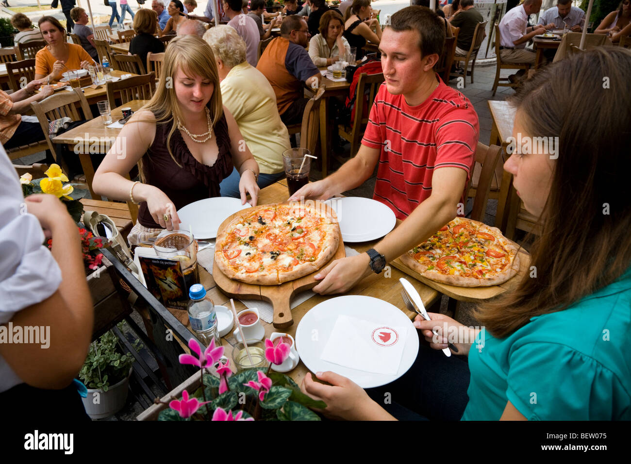 Les jeunes touristes anglais manger une pizza repas sur les tables de restaurant en plein air à la place du marché / Markt. Cracovie. La Pologne. Banque D'Images