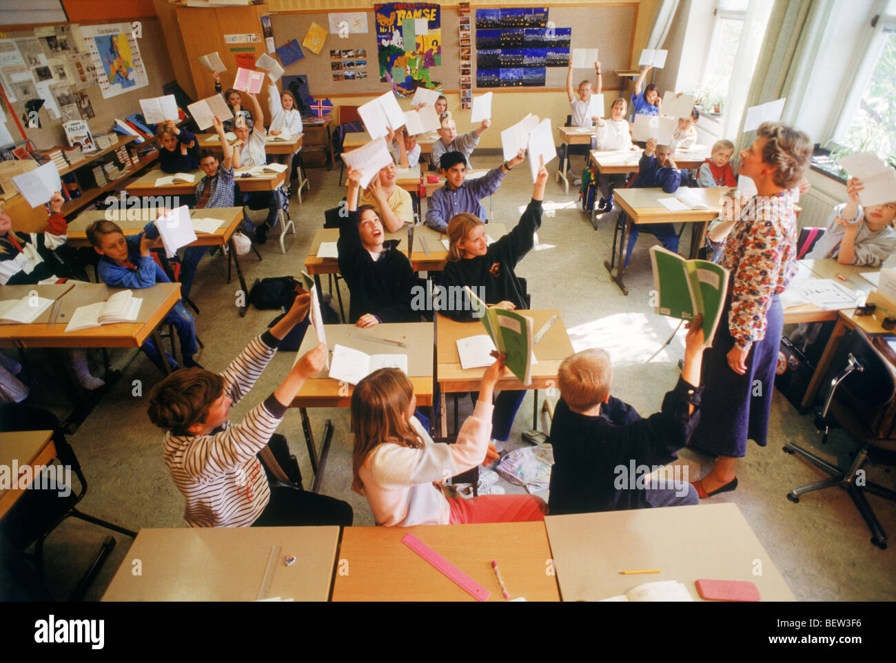 Les enfants de l'école élémentaire assis à un bureau individuel dans la classe suédois les mains pour répondre aux questions de l'enseignant Banque D'Images