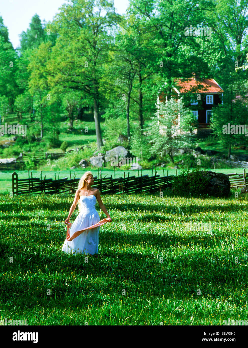 Femme blonde en robe blanche d'été de passage dans l'herbe verte de la Suède Banque D'Images