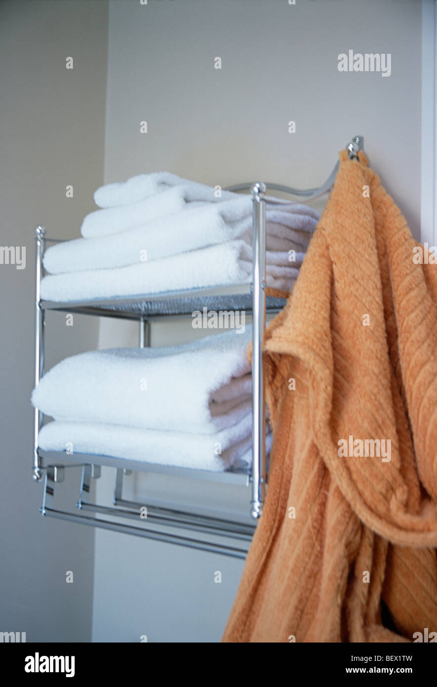 Close-up of orange peignoir en éponge sur les étagères en acier avec pile de serviettes blanches Banque D'Images