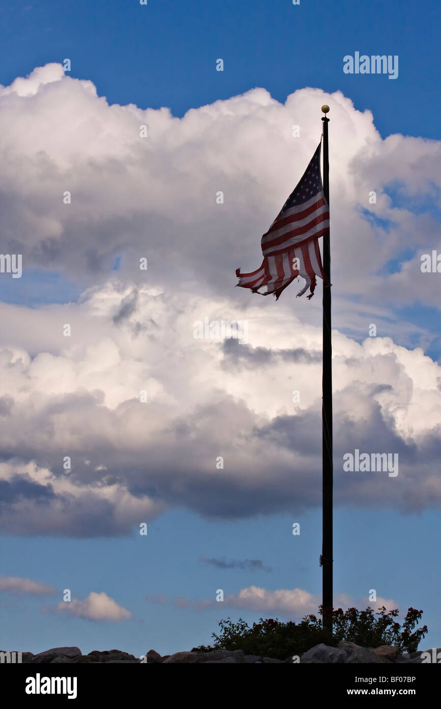 Drapeau américain qui est battue et déchiré sur un mât avec ciel bleu et nuages en arrière-plan. Banque D'Images