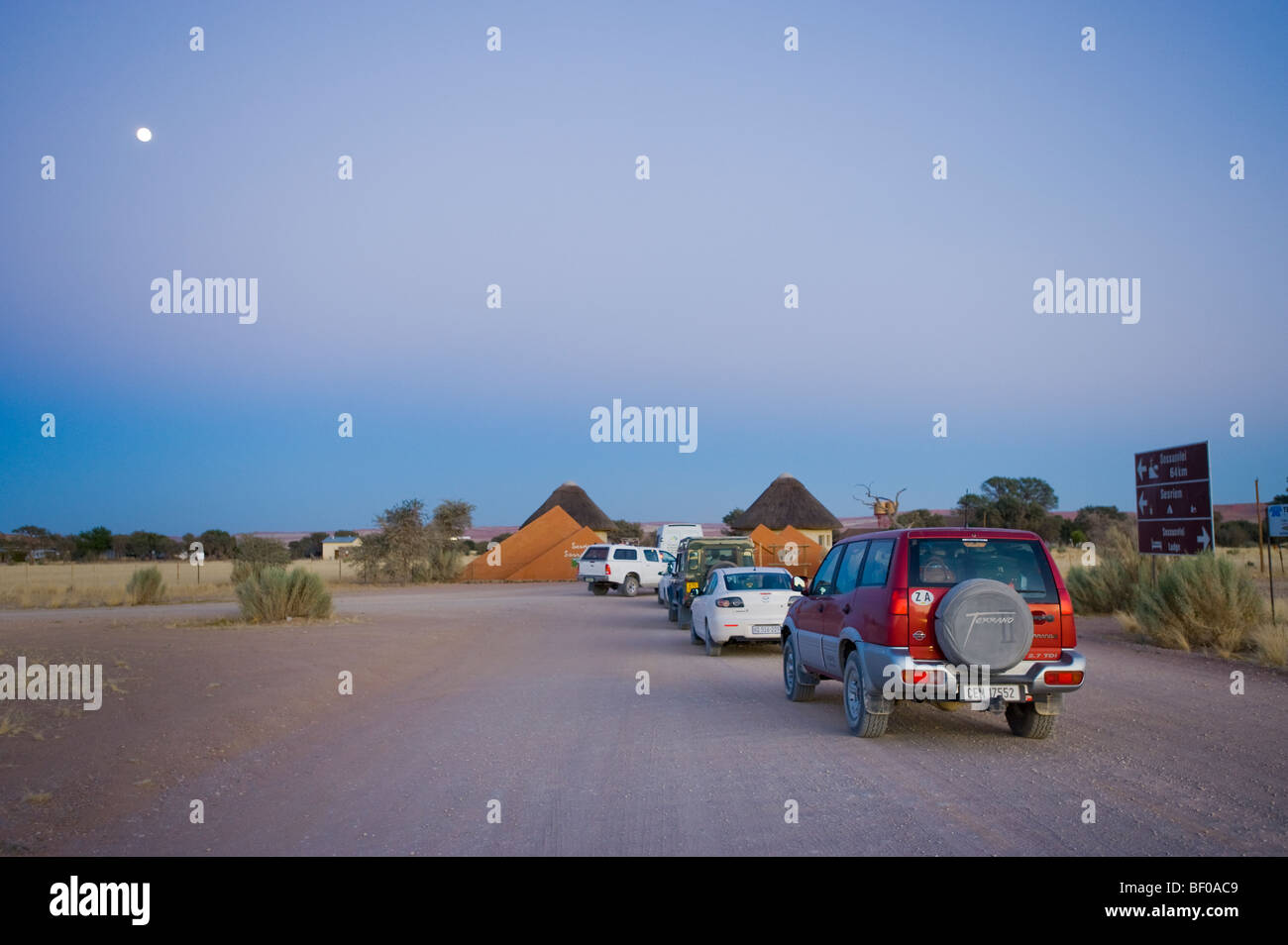 Voitures en attente à la porte pour l'ouverture de la Namibie Sesriem SOSSUSVLEI desert dunes route tôt le matin orange rouge jaune l'échelle de la poussière de sable Banque D'Images