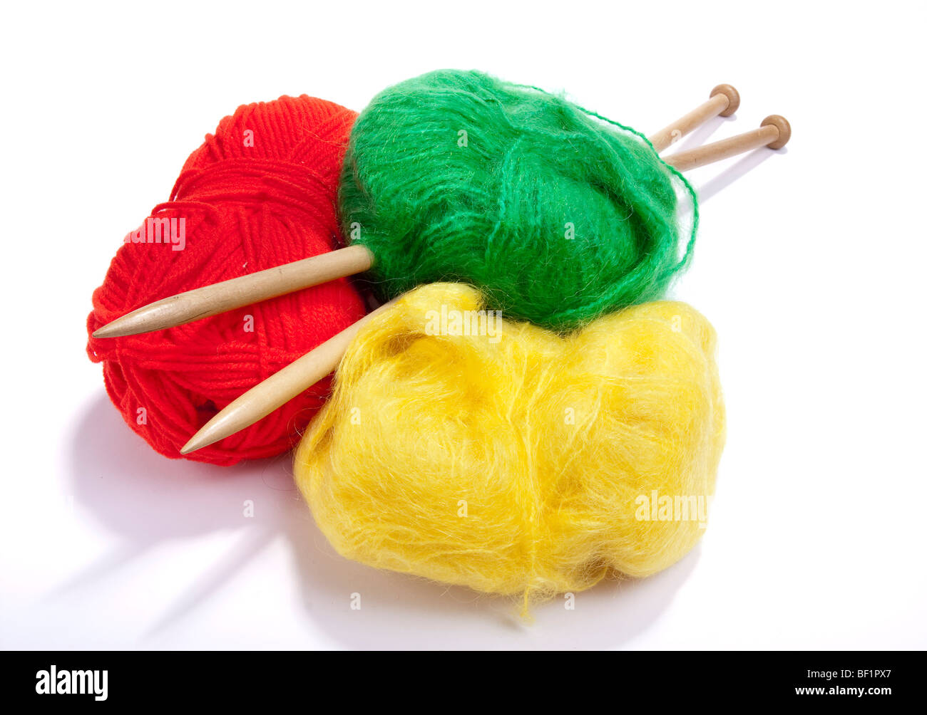 Gros ballon de rouge, jaune et vert laine mohair ou laine percé avec de grandes aiguilles à tricoter en bois contre l'arrière-plan blanc. Banque D'Images