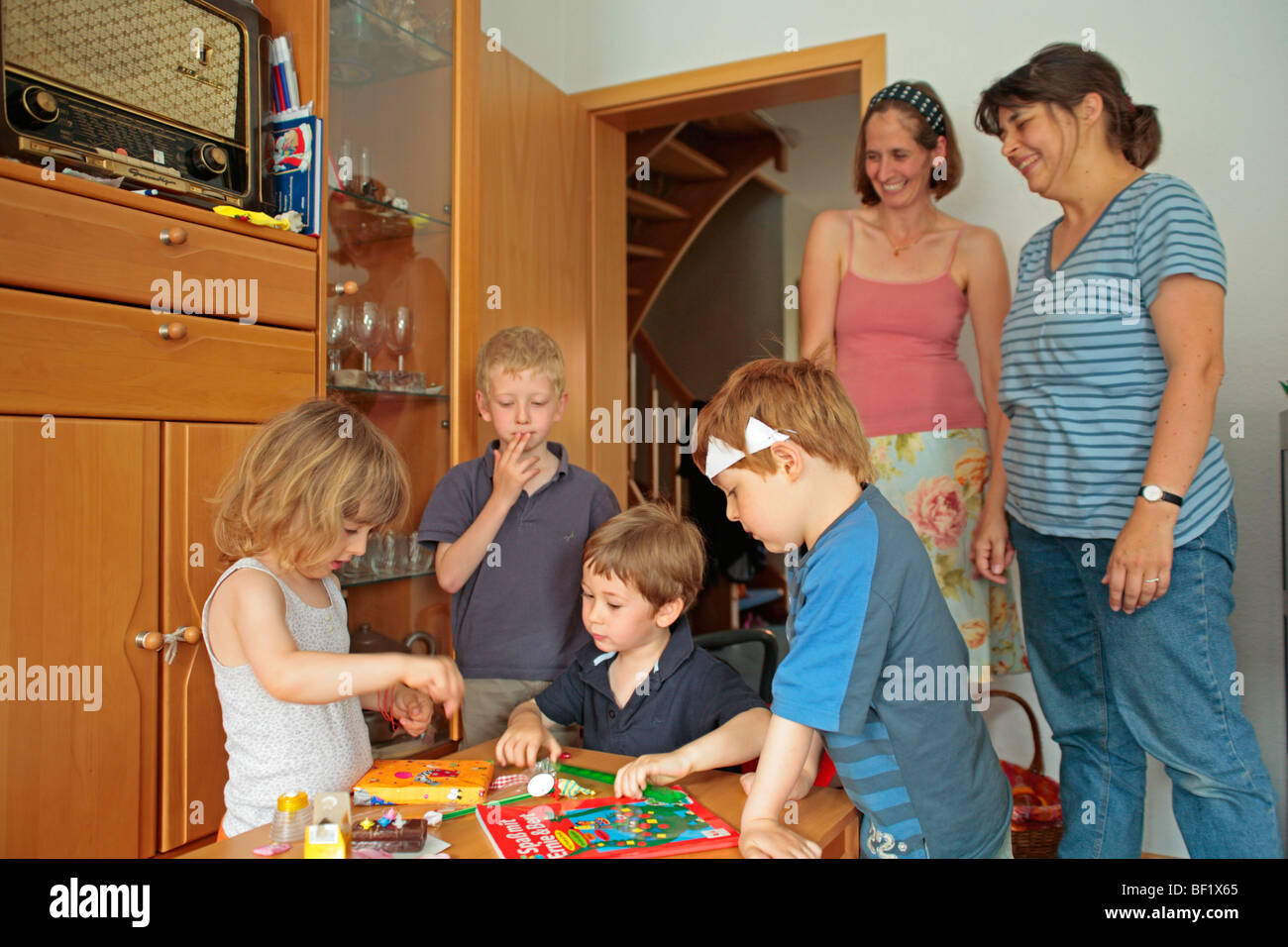 Une jeune fille d'ôter son présente à une fête d'anniversaire de l'enfant, les autres enfants à regarder Banque D'Images