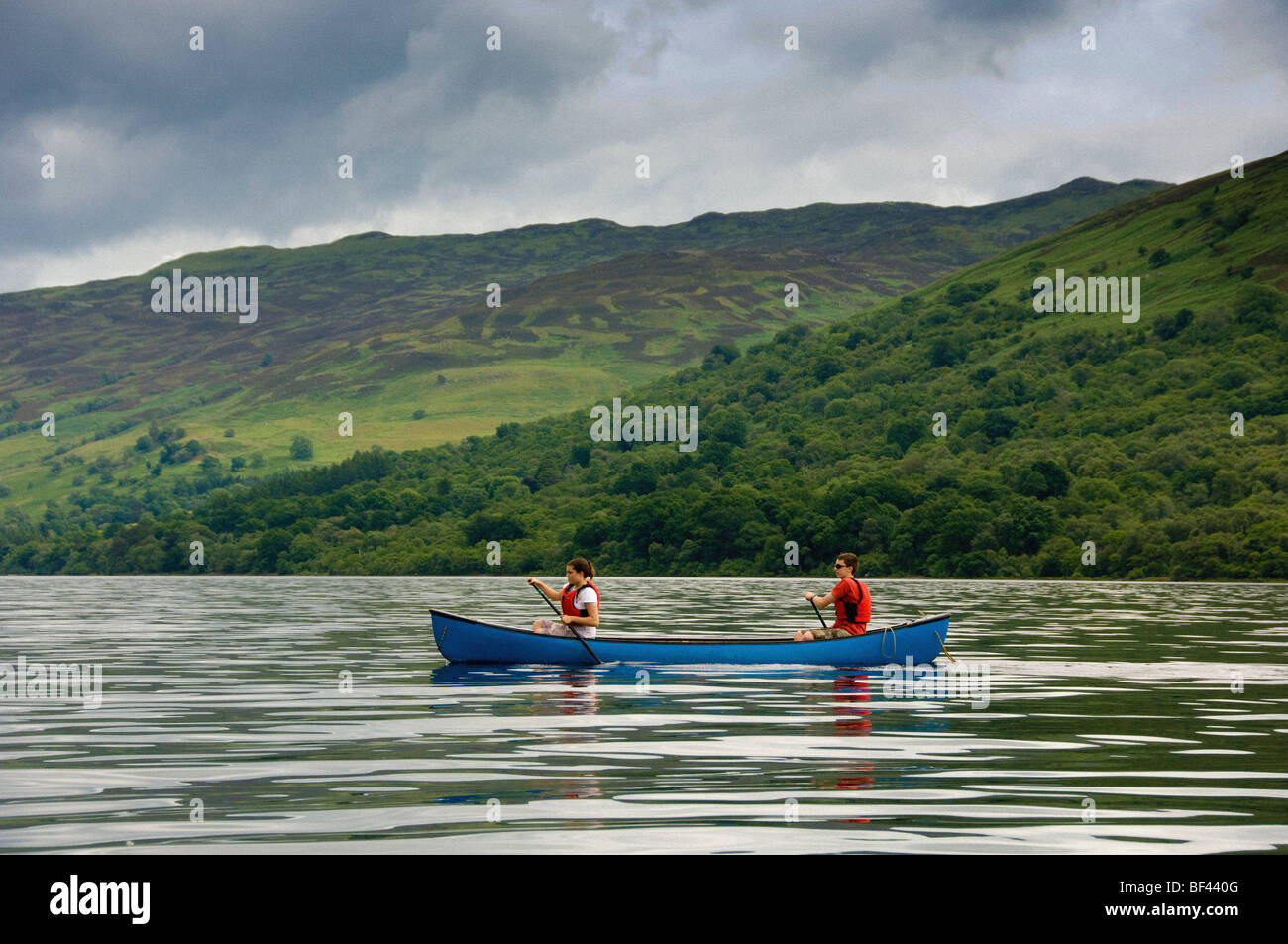 Vue latérale de 2 jeunes adultes du caucase pagayant un canot canadien sur un Loch Earn déserté, dans le Perthshire, en Écosse. ROYAUME-UNI Banque D'Images